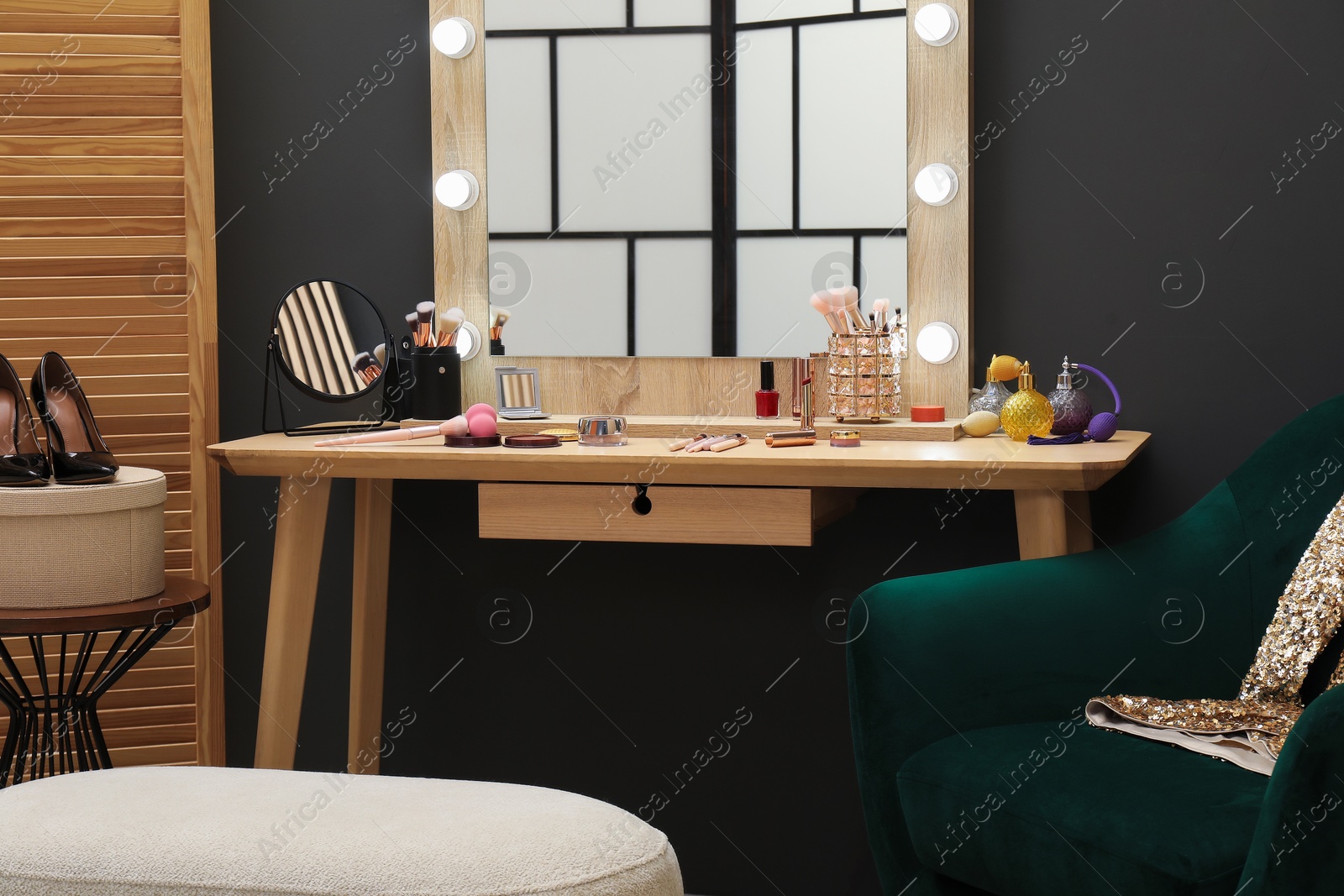 Photo of Makeup room. Wooden dressing table with mirrors, different beauty products, armchair and pouf indoors