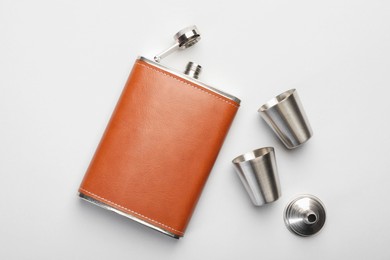 Photo of Hip flask, cups and funnel on white background, flat lay