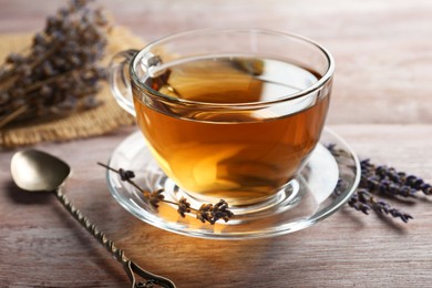 Photo of Aromatic lavender tea in glass cup, spoon and dry flowers on wooden table, closeup