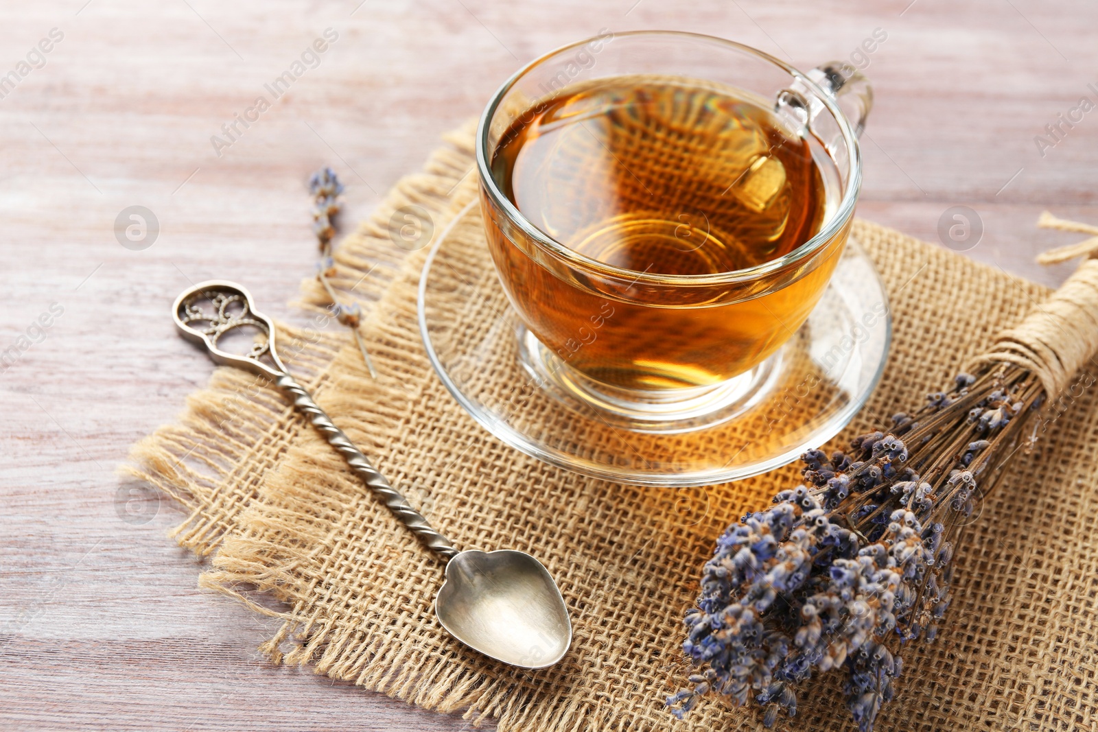 Aromatic lavender tea in glass cup, spoon and dry flowers on wooden table, closeup Photo of Aromatic lavender tea in glass cup, spoon and dry flowers on wooden table, closeup