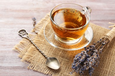 Photo of Aromatic lavender tea in glass cup, spoon and dry flowers on wooden table, closeup