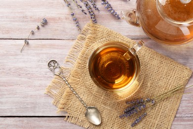 Photo of Aromatic lavender tea in glass cup, spoon and dry flowers on wooden table, flat lay