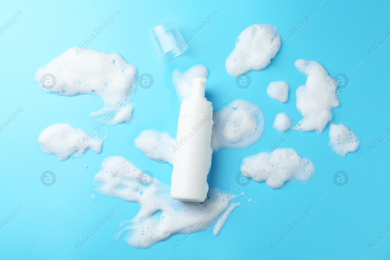 Photo of Bottle of cosmetic product with foam on light blue background, top view