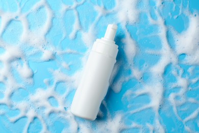 Photo of Bottle of cosmetic product with foam on light blue background, top view