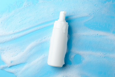 Bottle of cosmetic product with foam on light blue background, top view