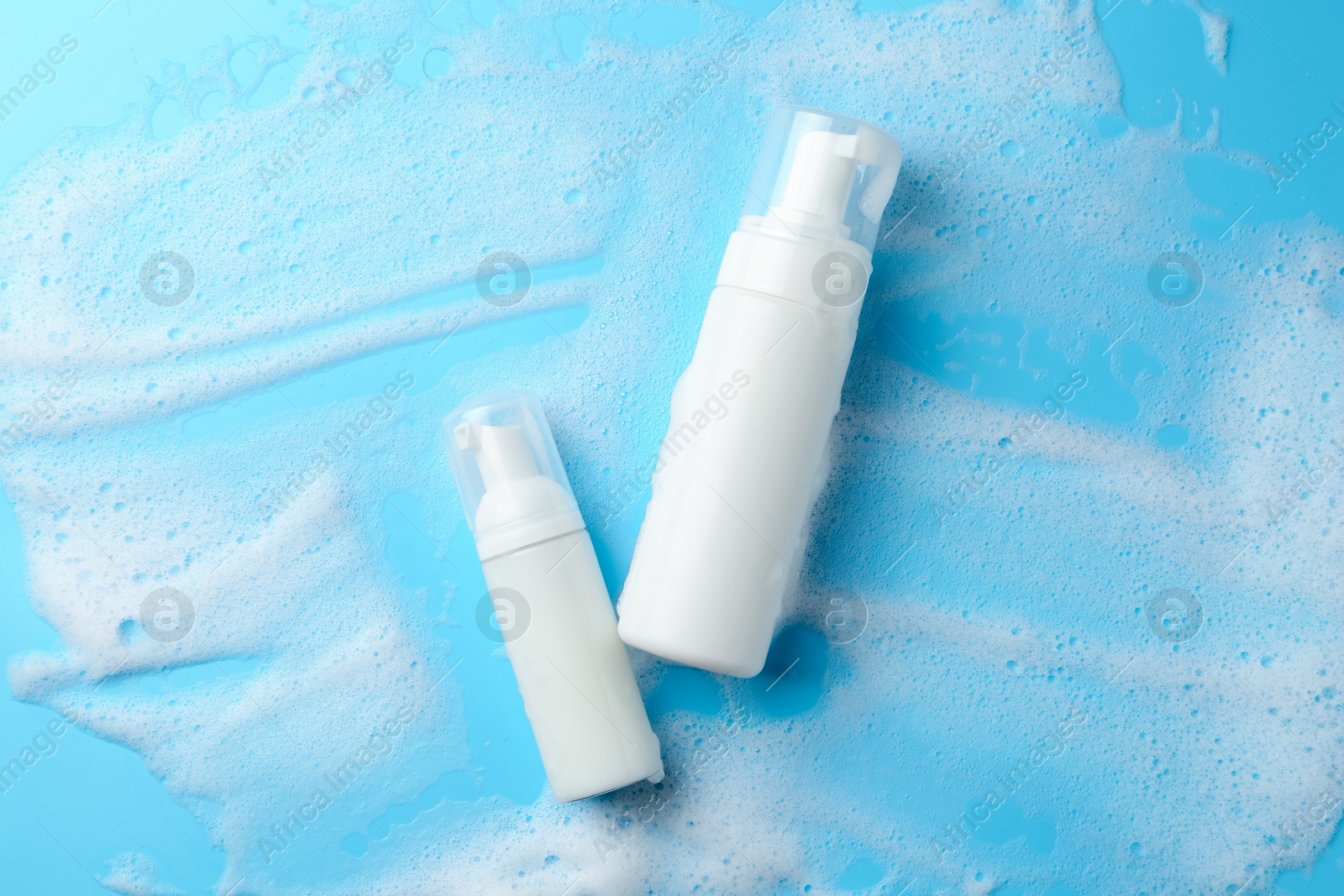 Photo of Bottles of cosmetic products with foam on light blue background, top view