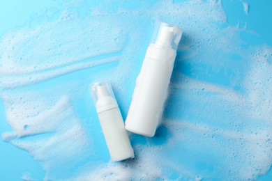 Bottles of cosmetic products with foam on light blue background, top view