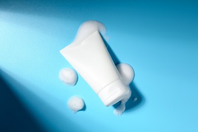 Photo of Tube of cosmetic product with foam on light blue background, top view