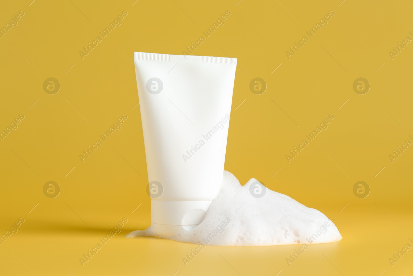 Photo of Tube of cosmetic product with foam on yellow background