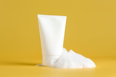 Photo of Tube of cosmetic product with foam on yellow background