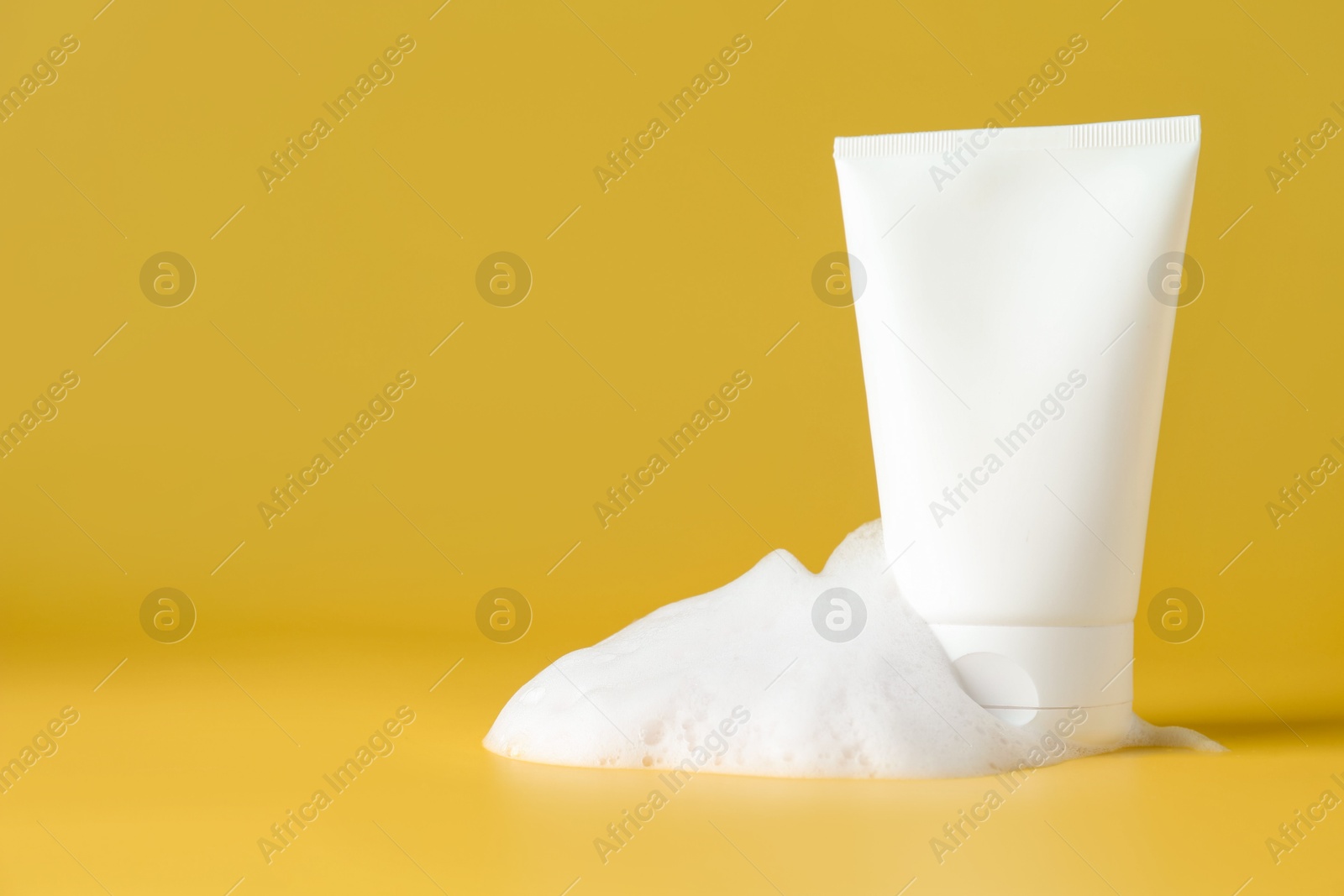 Photo of Tube of cosmetic product with foam on yellow background, space for text