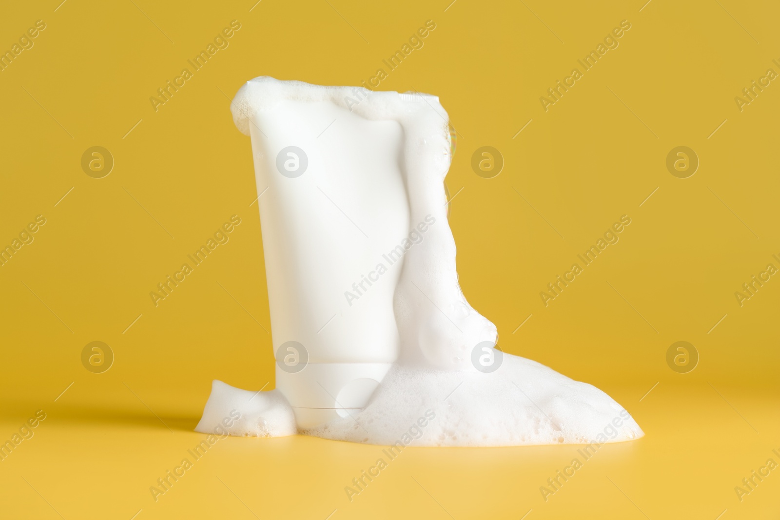 Photo of Tube of cosmetic product with foam on yellow background