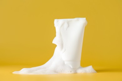 Photo of Tube of cosmetic product with foam on yellow background