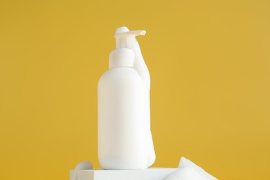 Bottle of cosmetic product with foam on podium against yellow background