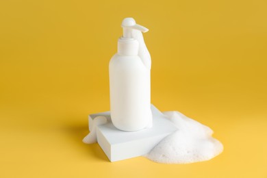 Photo of Bottle of cosmetic product with foam on podium against yellow background