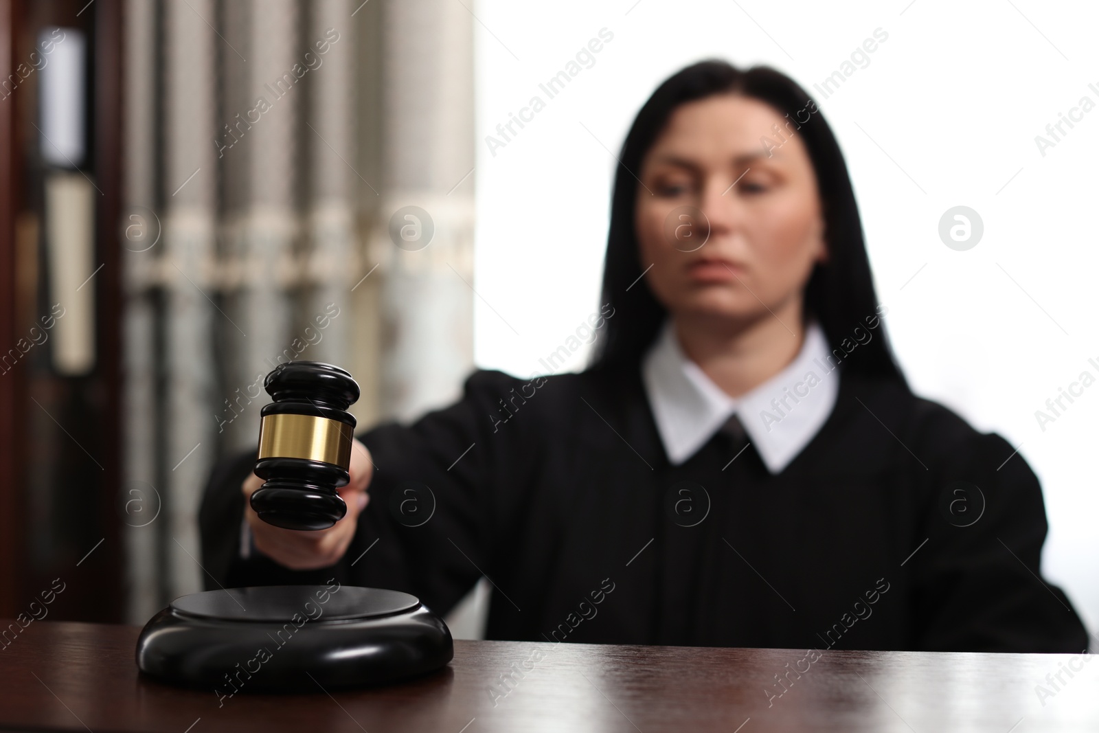 Photo of Judge striking gavel at wooden table in courtroom, selective focus