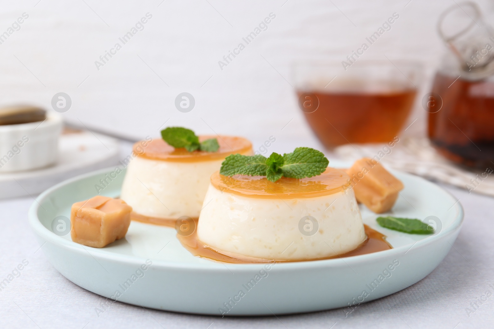 Photo of Tasty puddings with caramel sauce served on white table, closeup