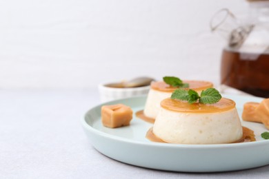 Photo of Tasty puddings with caramel sauce served on white table, closeup. Space for text