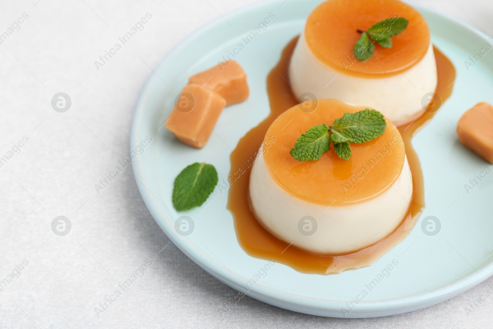 Photo of Tasty puddings with caramel sauce served on white table, closeup. Space for text