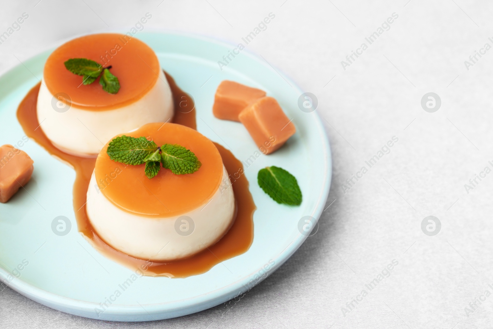 Photo of Tasty puddings with caramel sauce served on white table, closeup. Space for text