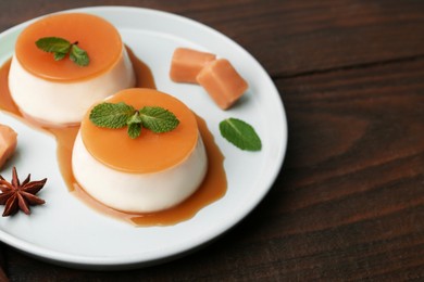 Photo of Tasty puddings with caramel sauce served on wooden table, closeup. Space for text