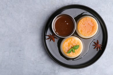 Photo of Tasty puddings with caramel sauce served on light grey table, top view. Space for text