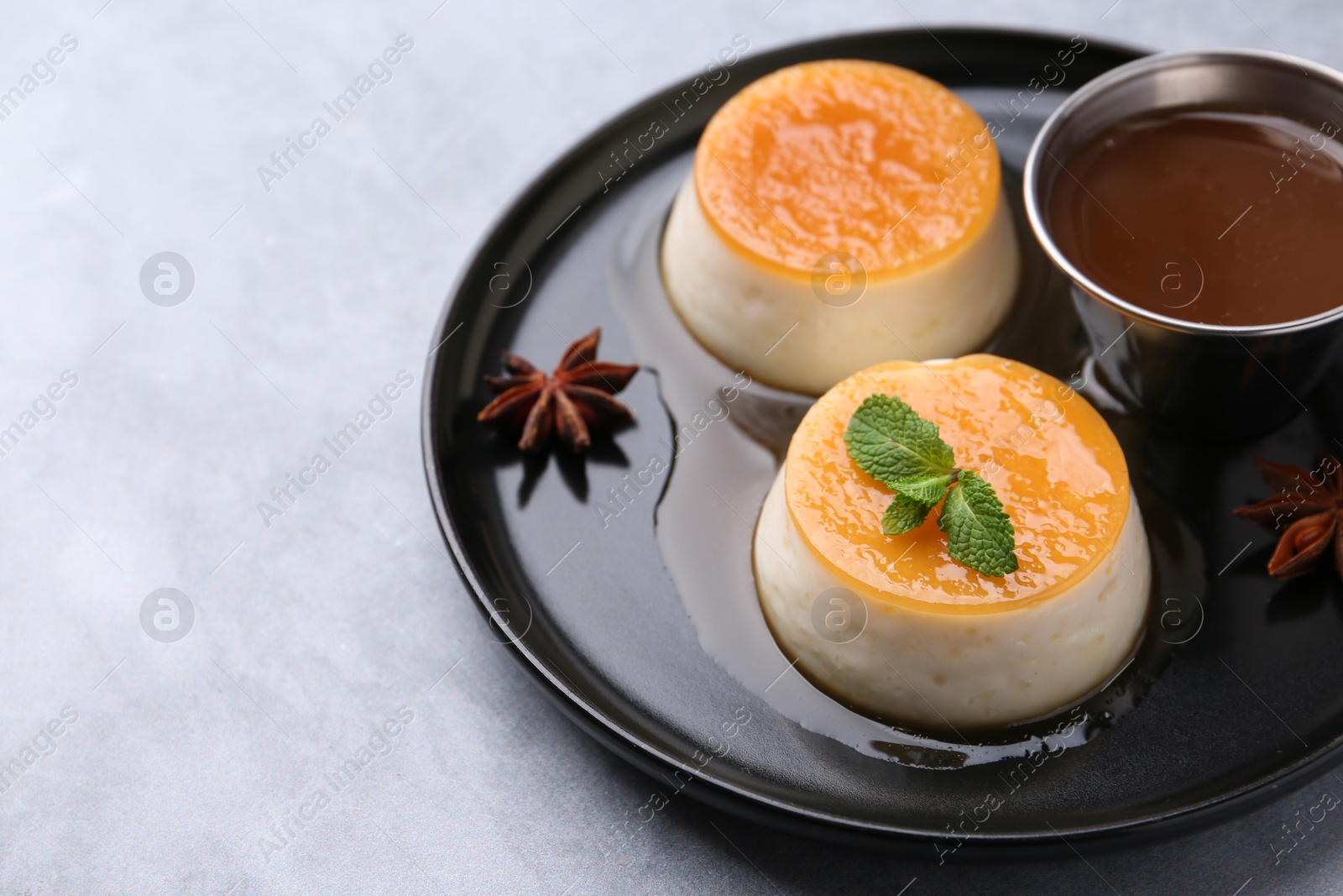 Photo of Tasty puddings with caramel sauce served on light grey table, closeup. Space for text