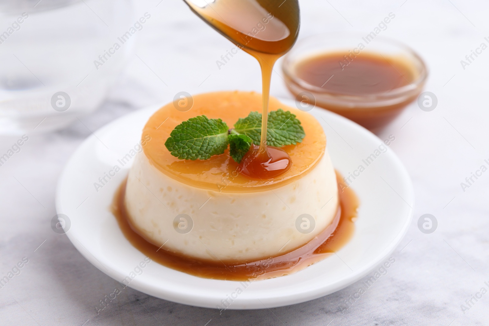 Photo of Tasty pudding with caramel sauce served on white marble table, closeup