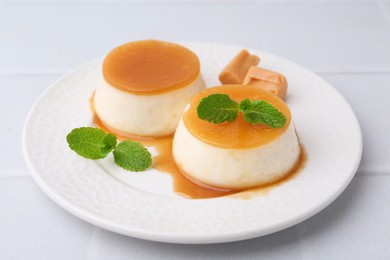 Photo of Tasty puddings with caramel sauce served on white tiled table, closeup