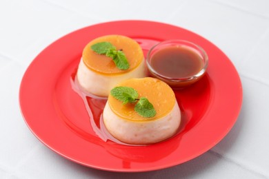 Photo of Tasty puddings with caramel sauce served on white tiled table, closeup