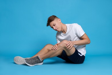 Photo of Young man suffering from pain in knee on light blue background