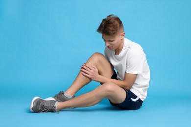 Photo of Young man suffering from pain in knee on light blue background