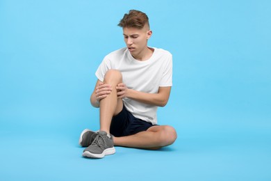 Photo of Young man suffering from pain in knee on light blue background