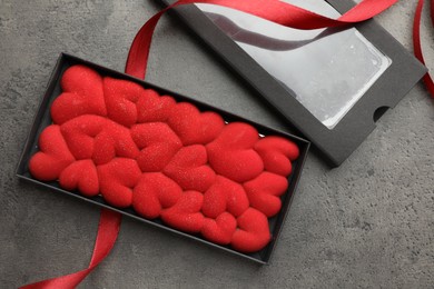 Photo of Chocolate bar decorated with hearts in box and red ribbon on grey table, flat lay