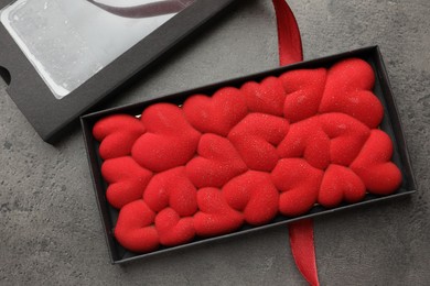 Photo of Chocolate bar decorated with hearts in box and red ribbon on grey table, flat lay