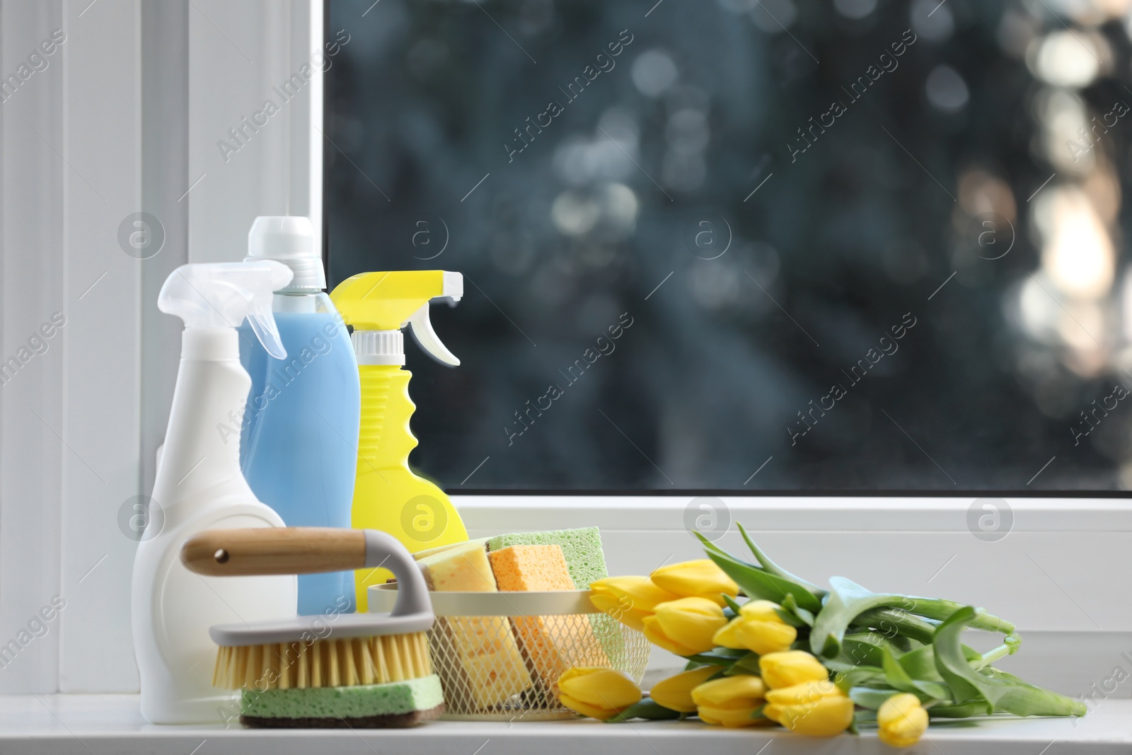 Photo of Spring cleaning. Detergents, supplies and yellow tulips near window indoors