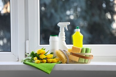 Photo of Spring cleaning. Detergents, supplies and yellow tulips near window indoors