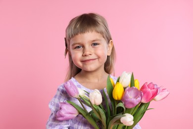 Photo of Cute little girl with bouquet of tulips on pink background