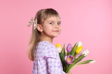 Photo of Cute little girl with bouquet of tulips on pink background