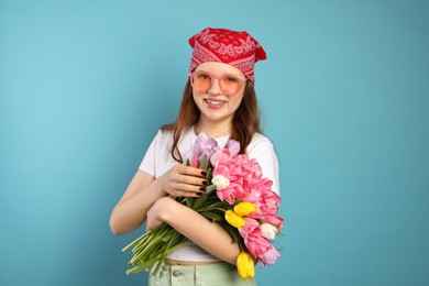 Photo of Beautiful teenage girl with bouquet of tulips on light blue background