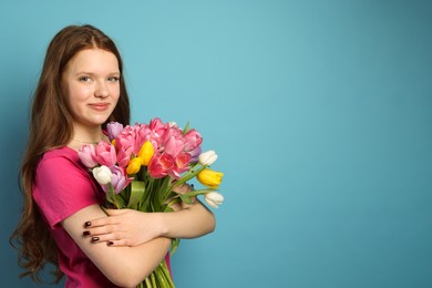 Photo of Beautiful teenage girl with bouquet of tulips on light blue background, space for text