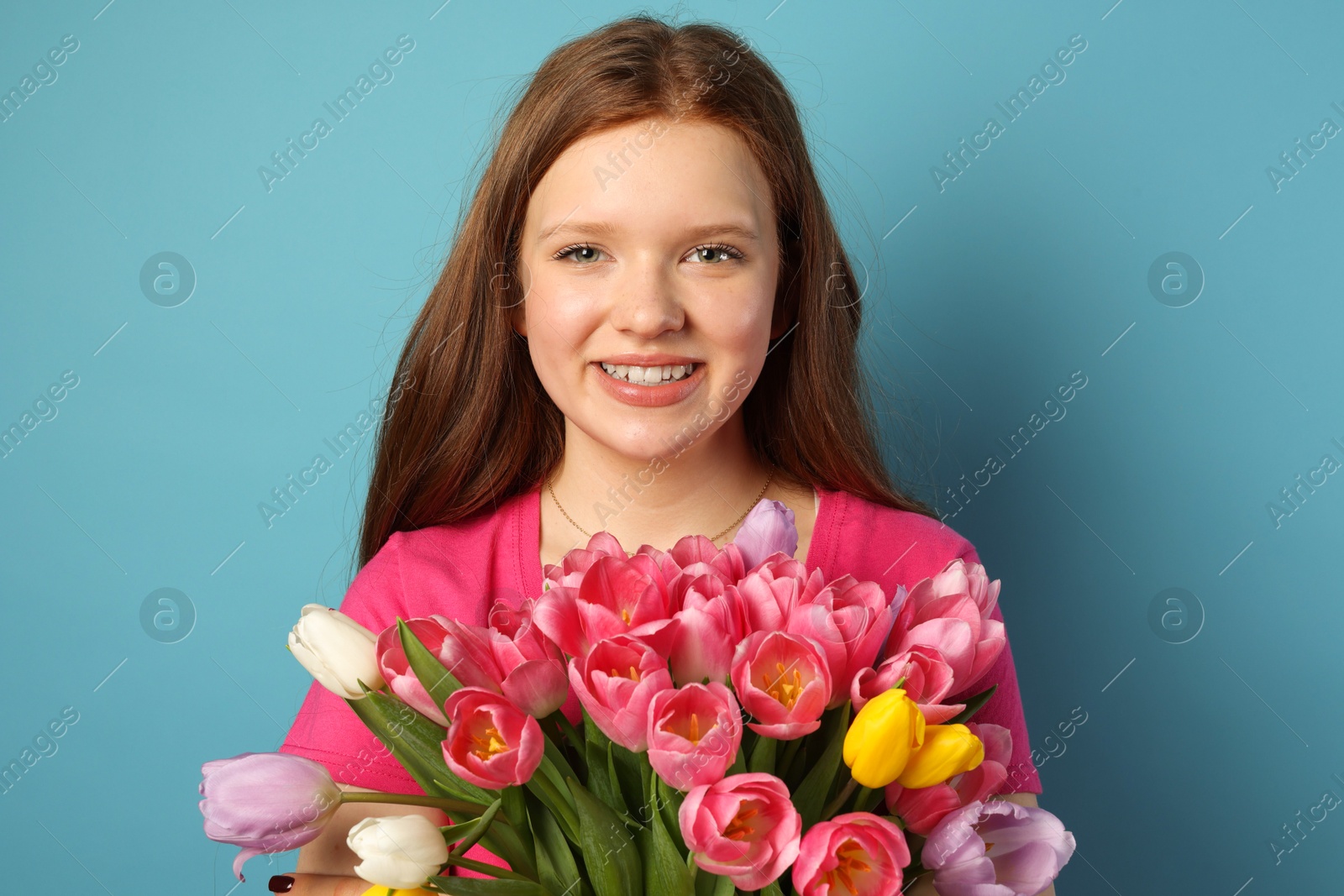 Photo of Beautiful teenage girl with bouquet of tulips on light blue background