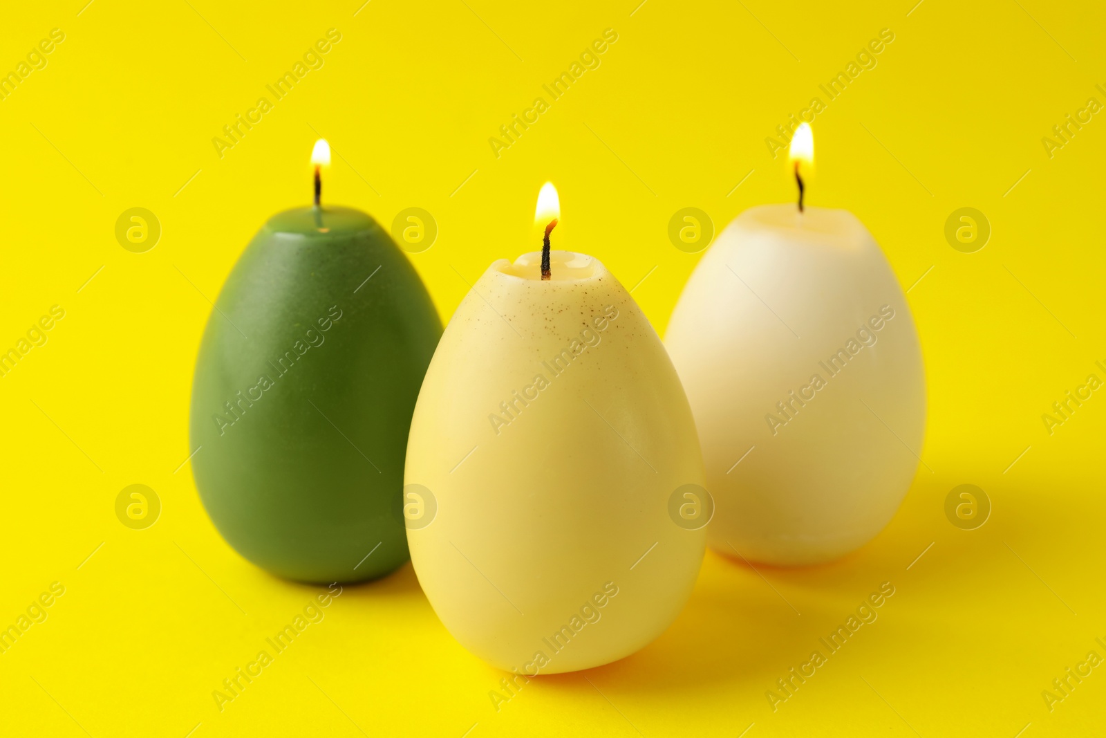 Photo of Beautiful burning egg shaped candles on yellow background, closeup. Easter decor