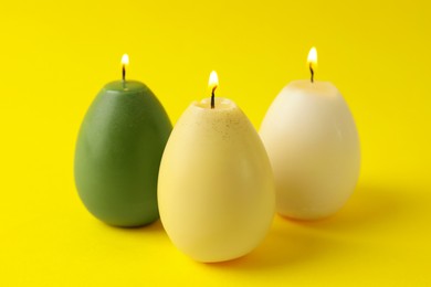 Photo of Beautiful burning egg shaped candles on yellow background, closeup. Easter decor