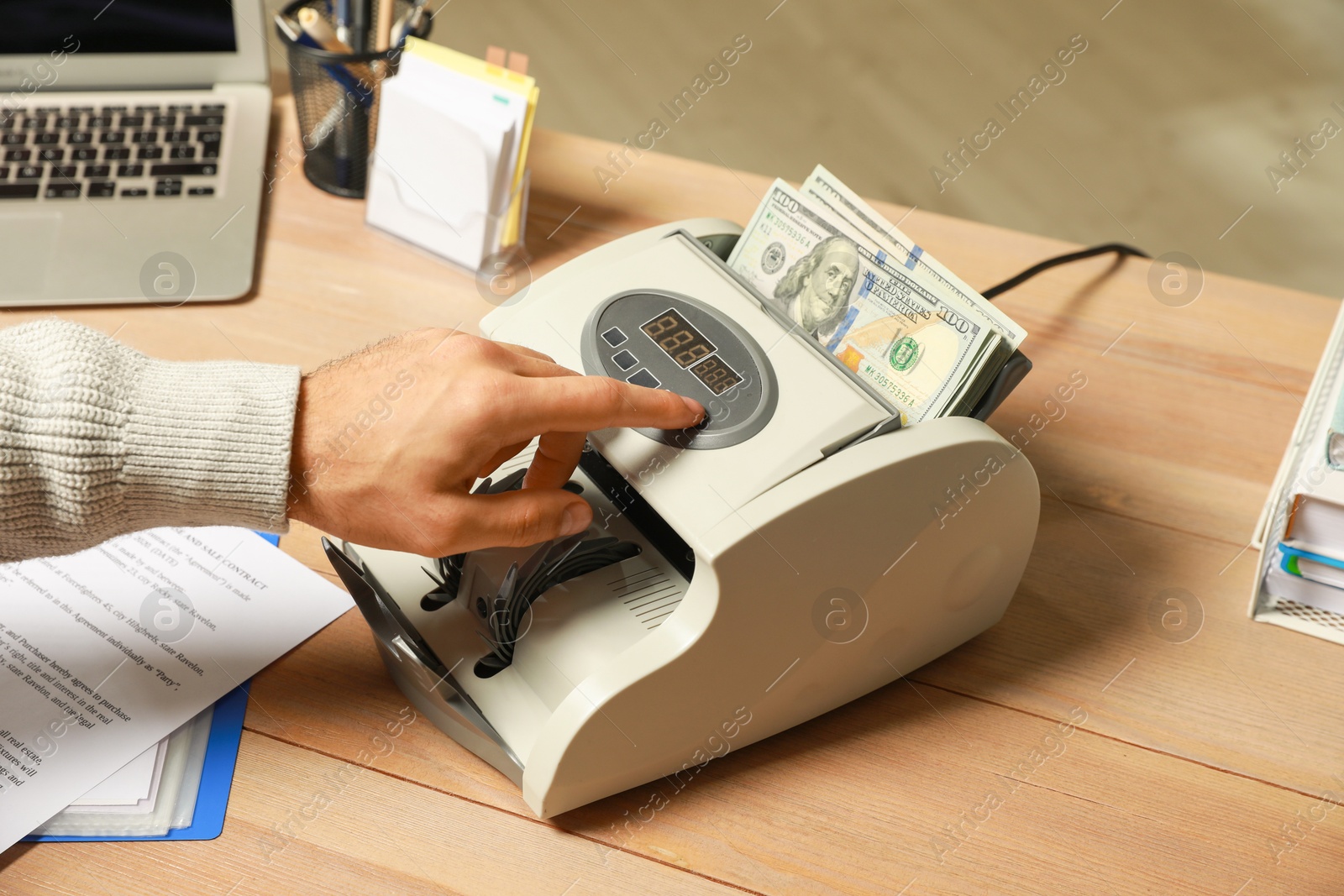 Photo of Man using banknote counter at wooden table indoors, closeup