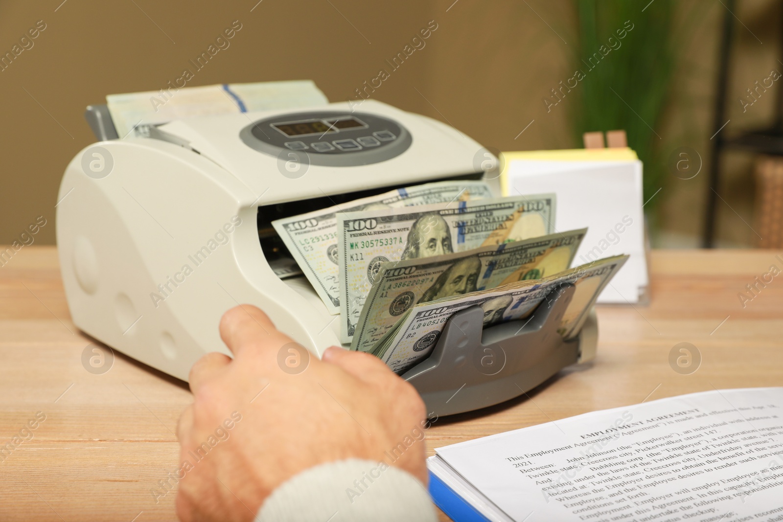 Photo of Man using banknote counter at wooden table indoors, closeup