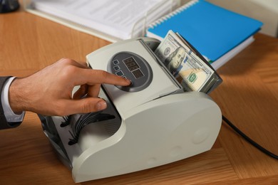 Photo of Man using banknote counter at wooden table, closeup