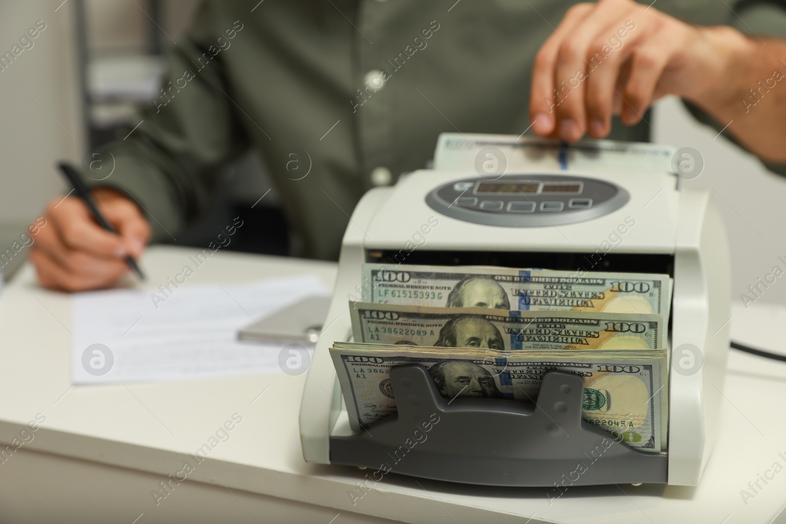 Photo of Man using banknote counter at white table indoors, closeup