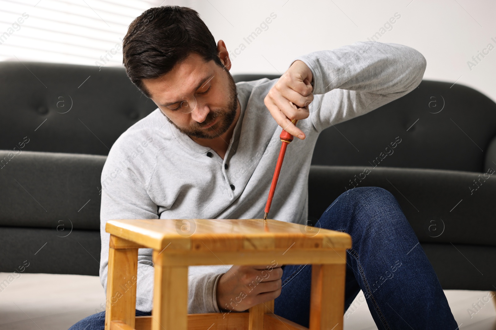 Photo of Man repairing wooden stool with screwdriver at home