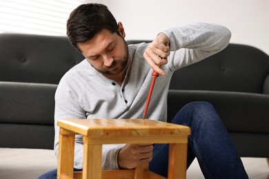 Photo of Man repairing wooden stool with screwdriver at home